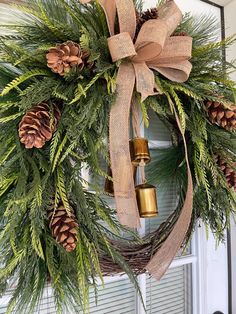 a wreath with pine cones and bells hanging on the front door