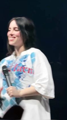 a woman holding a microphone in her right hand and wearing a white t - shirt