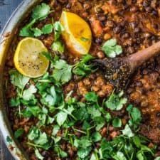 a pot filled with beans and cilantro on top of a wooden table next to two lemon wedges