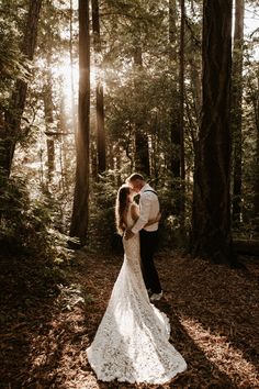 a bride and groom standing in the woods at their outdoor wedding ceremony with sun shining through the trees