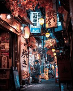 a man sitting on the ground in front of a building with lanterns hanging from it