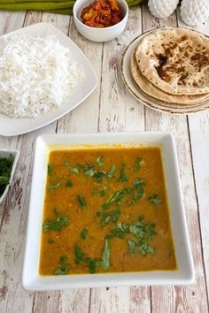 there are many different foods on the table including rice, bread and vegetables in bowls