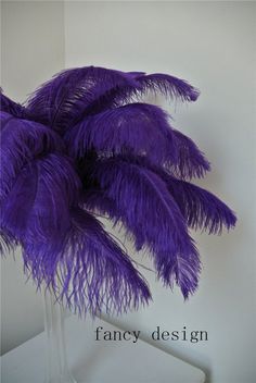 purple ostrich feathers in a glass vase on a white table with the words fancy design above it