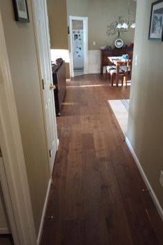 an empty hallway with hard wood floors and white trim on the walls, leading to a dining room