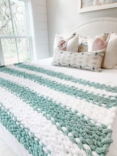 a white bed with blue and green crocheted bedspread next to a window