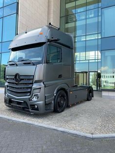 a mercedes semi truck parked in front of a building with glass windows on the side