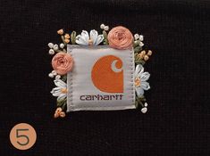 an orange and white patch with flowers in the center on a black shirt that says canaant