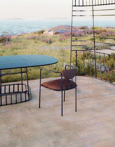 two chairs and a table on a patio overlooking the ocean with purple wildflowers