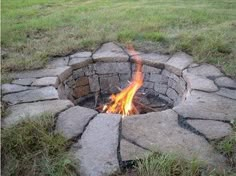 an open fire pit in the middle of a field with grass and rocks around it