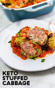 a white plate topped with stuffed cabbage covered in marinara sauce next to a casserole dish