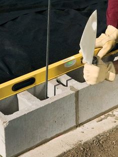 a person with gloves on holding a large knife in front of some concrete block walls