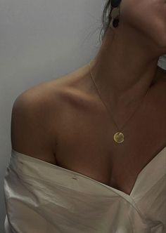 a woman wearing a white dress with a gold disc necklace on her neck and earrings