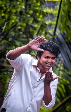 a man standing in front of some trees making the vulcan sign with his hands and smiling