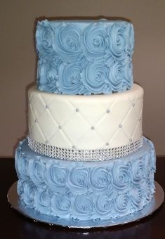 three tiered cake with blue frosting and white icing roses on each layer