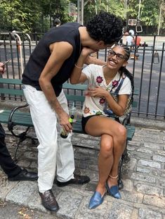 a woman sitting on top of a green bench next to a man in white pants