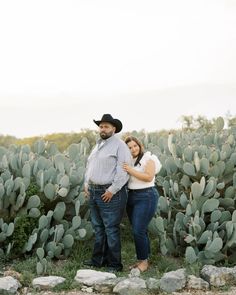 a man and woman standing next to each other in front of a cactus field with lots of cacti