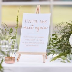 a sign sitting on top of a table next to vases filled with flowers and greenery