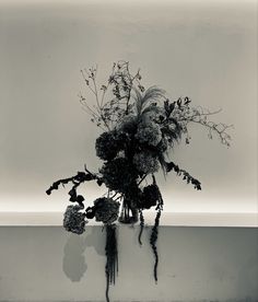 a black and white photo of flowers in a vase on a table with water reflection