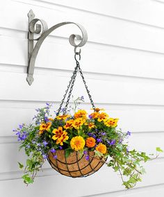 a hanging basket filled with flowers on the side of a white house next to a metal hook