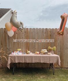 a party table with balloons and cake in the shape of animals on it, next to a fence