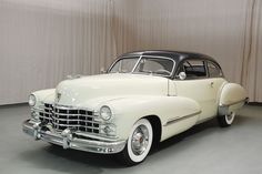 an old white car is parked in a room with drapes on the wall behind it