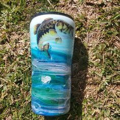 a glass vase with a fish painted on it sitting in the middle of some grass