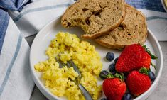 a white plate topped with eggs, toast and strawberries