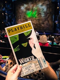 a person holding up a playbill ticket in front of a crowd at a theater