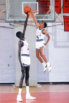 two young men playing basketball in an indoor gym, one jumping up to dunk the ball