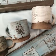 two coffee mugs sitting next to each other in front of a mirror with trees on them