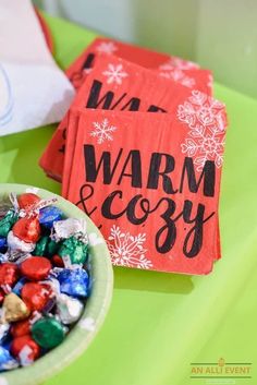 a bowl filled with candy next to a napkin that says warm & cozy on it