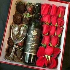 a wine bottle and some chocolates in a box with roses on the table next to it