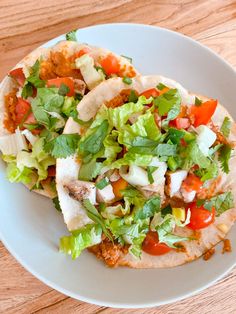 two tacos with lettuce, tomatoes and other toppings on a white plate