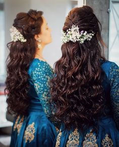 two women in blue dresses looking at each other with long hair and flowers on their head