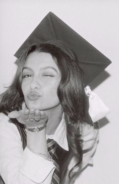 a woman wearing a graduation cap and holding her hand up to her mouth while standing in front of a white wall