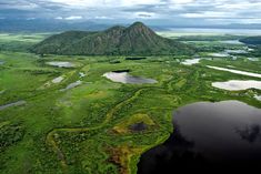 an aerial view of a lake surrounded by lush green land and mountains in the distance