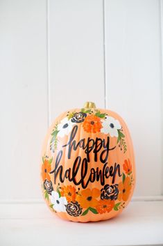 an orange painted pumpkin with the words happy halloween written on it and flowers around it