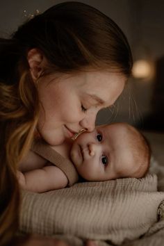 a woman holding a baby in her arms and kissing it's face with both hands