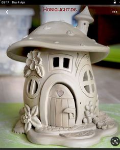 a small white house with flowers and mushrooms on it's roof, sitting on a table