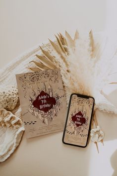 an open book sitting on top of a table next to a cell phone and feather