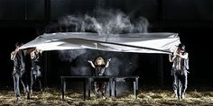 three people standing under a white sheet on top of a table in the middle of a dark room