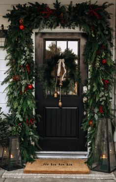 a christmas wreath on the front door of a house decorated with greenery and bells