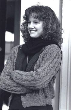 a black and white photo of a woman with her arms crossed, standing in front of a building