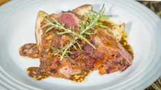 a white plate topped with meat covered in gravy and garnished with herbs