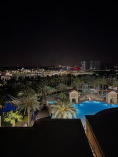 an aerial view of the pool at night with palm trees and buildings in the background