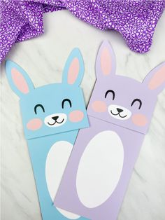 two bunny paper puppets sitting next to each other on a white surface with purple and blue patterns