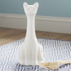 a white ceramic cat figurine sitting on top of a blue and white rug