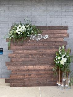 two vases filled with flowers and greenery on top of a wooden board wall