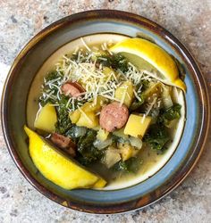 a bowl of soup with sausage, kale and lemon slices on the table top