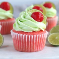 cupcakes with green frosting and cherries on top, surrounded by lime slices